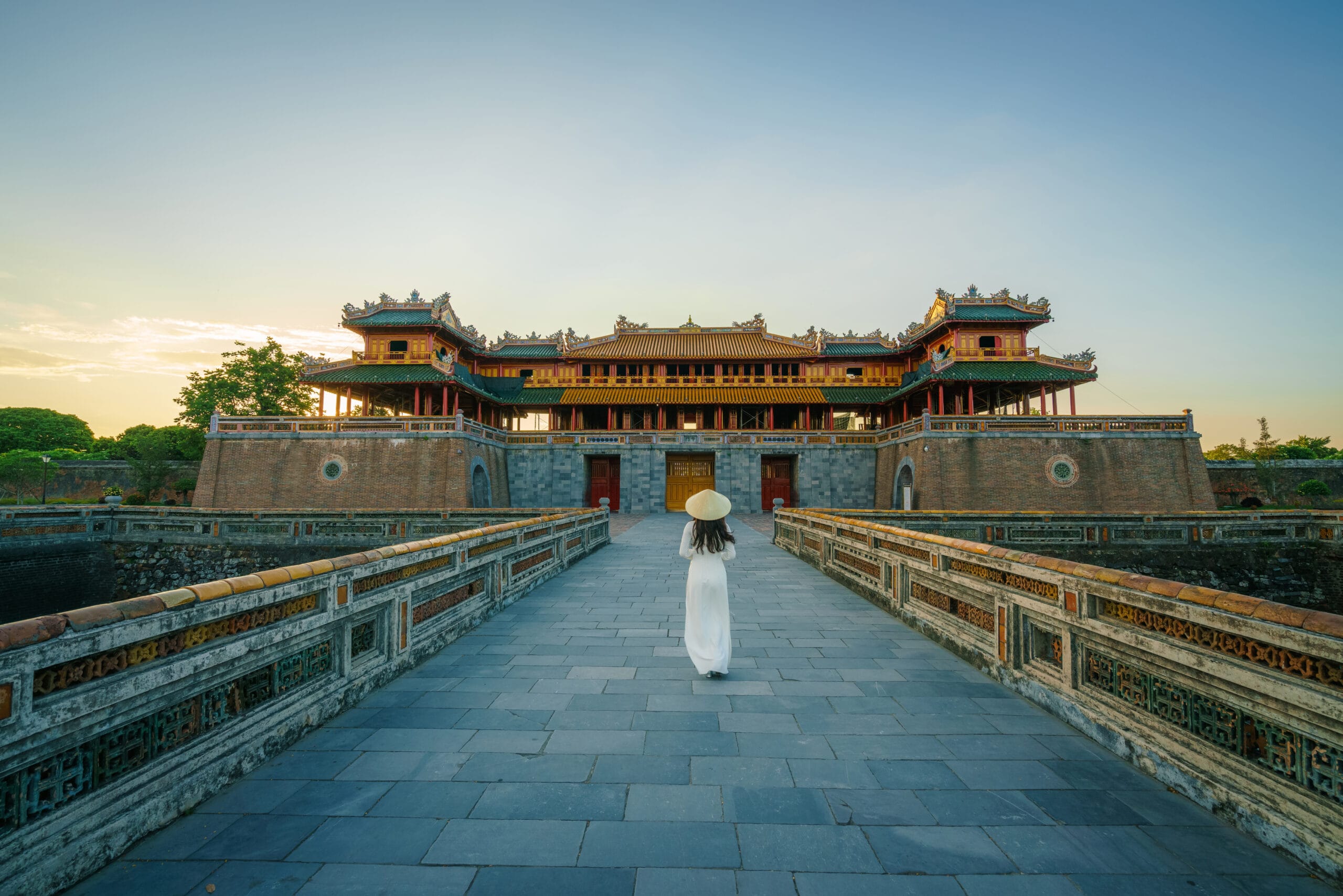 woman wearing white ao Dai walking on Ngo Mon gate at the entrance of the forbidden Hue Imperial City in Hue, Vietnam