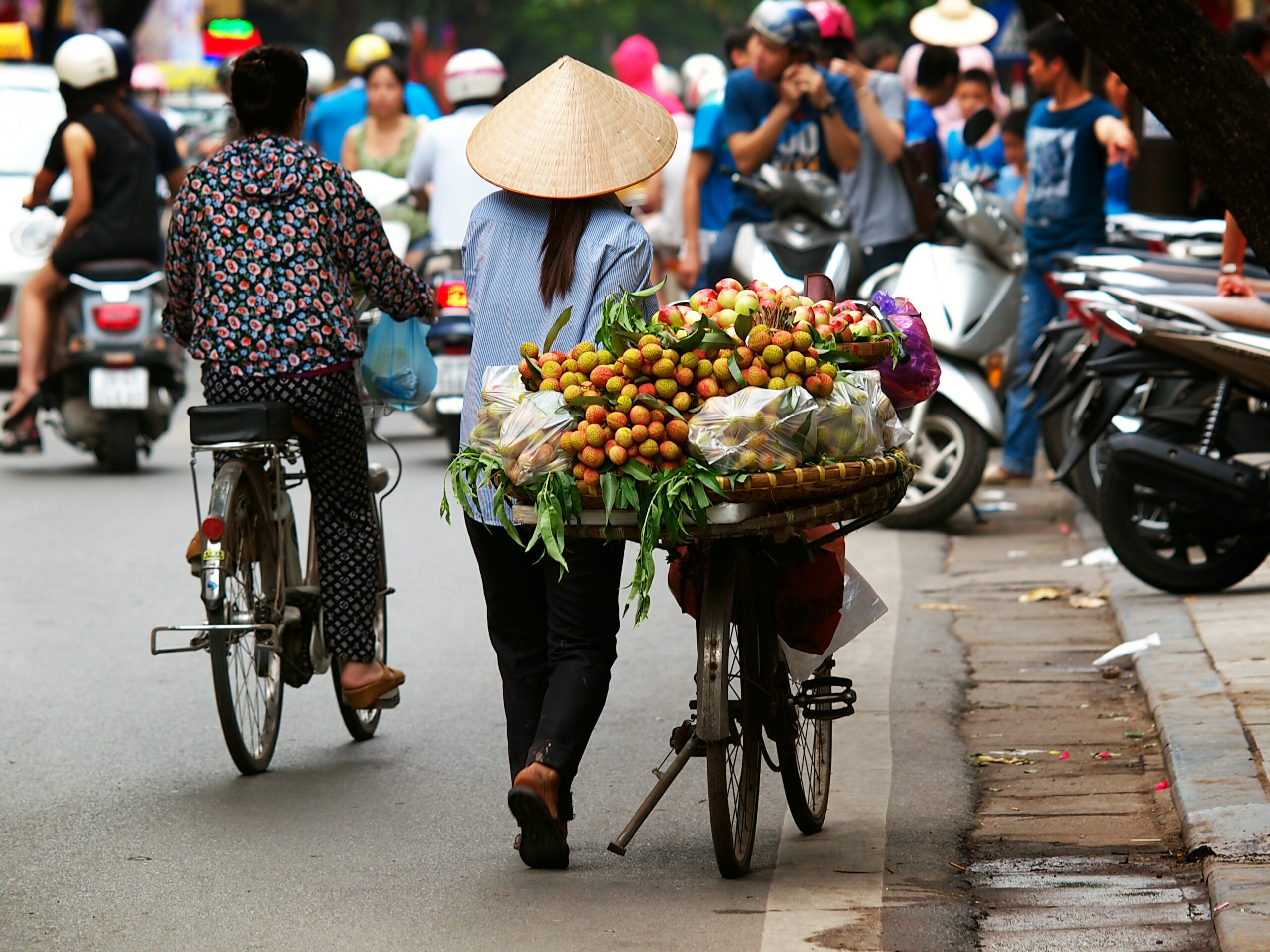 street vendor pushing bike full of fruits on a busy street